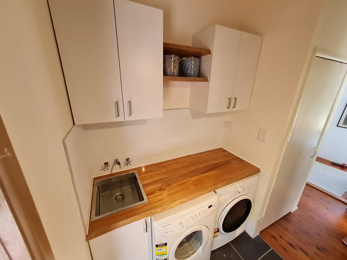 Renovated laundry with white overhead cabinets, timber benchtop and subway splashback