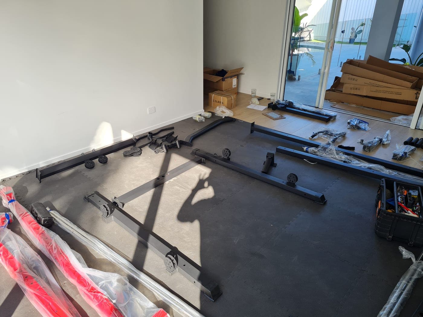 Home gym rack in pieces laid out on the rubber floor with the fixings sorted