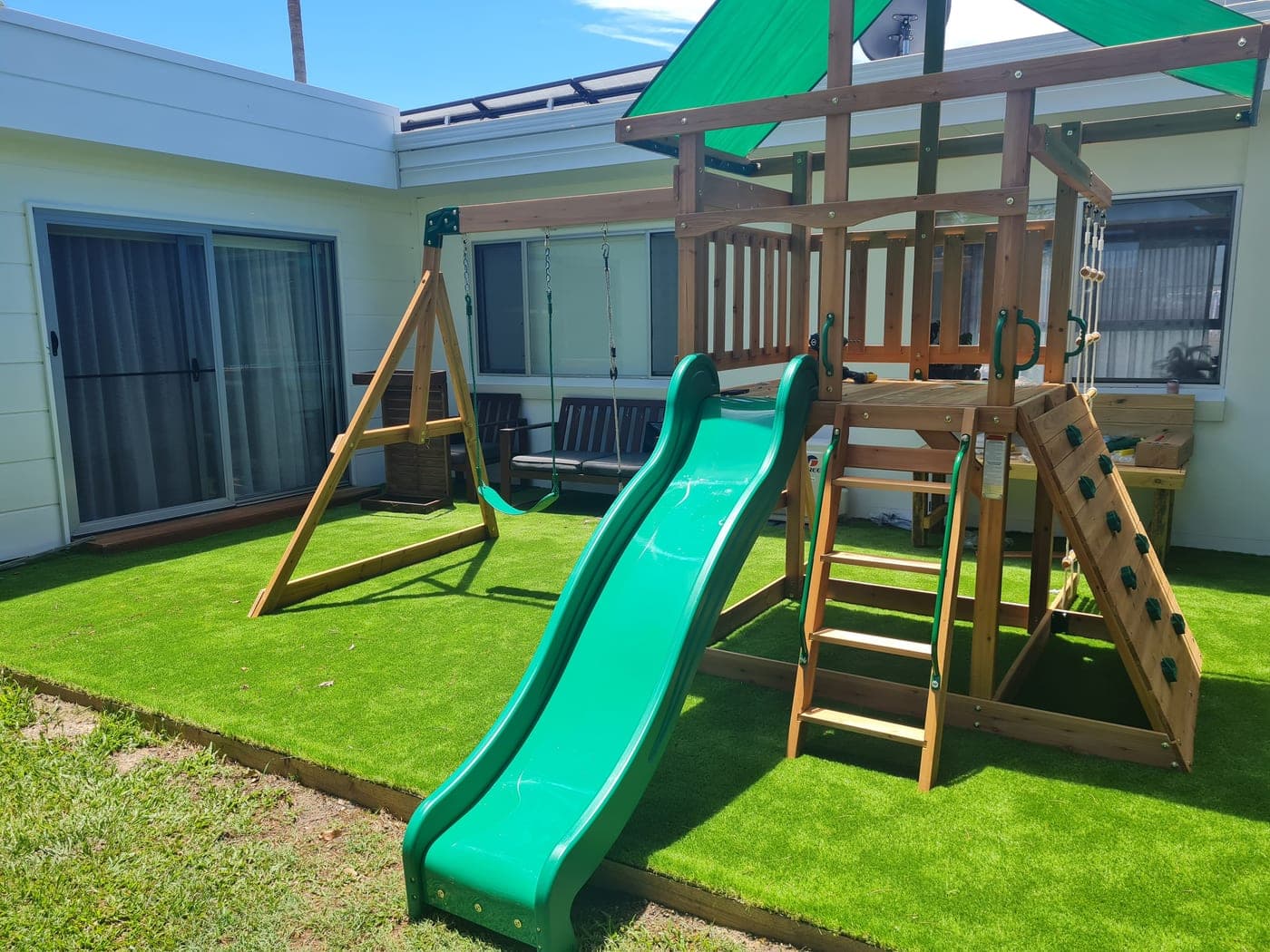 Finished timber playset with slide, swings and climbing wall on the lawn
