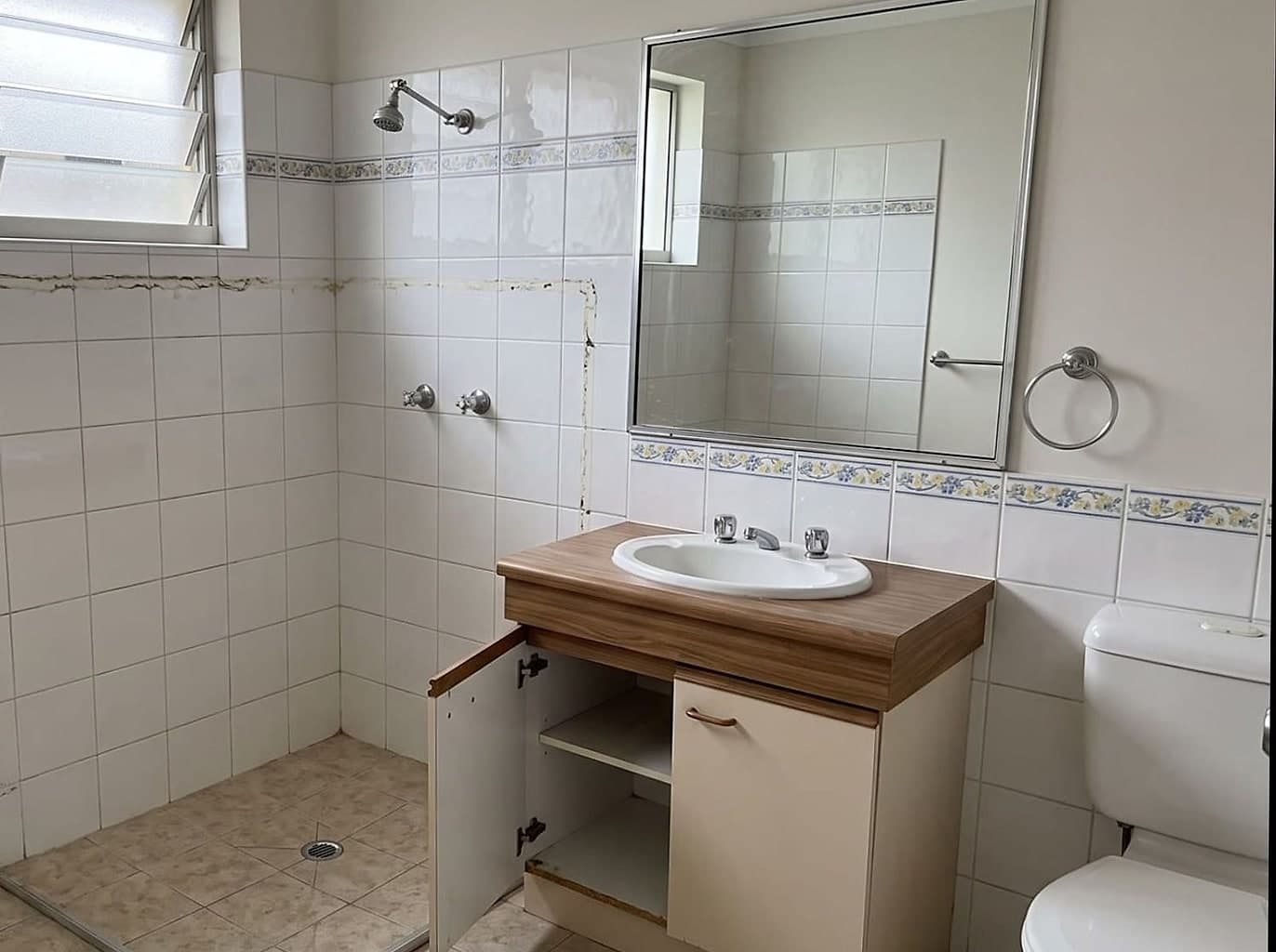 Dated unit bathroom cleared for work, the old shower screen taken out and a vanity door removed