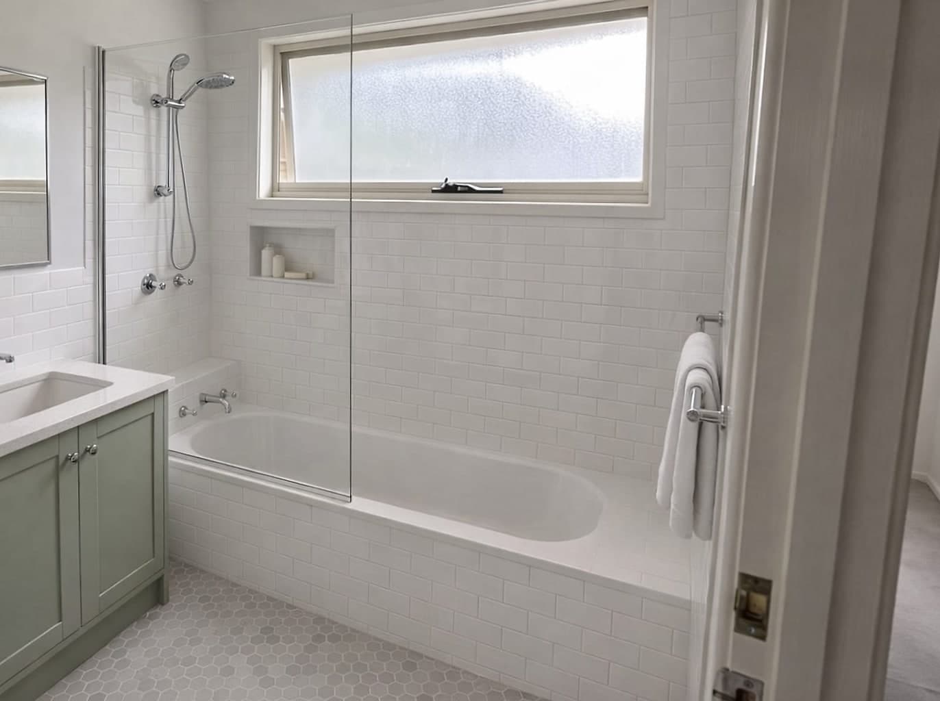 The same bathroom re-tiled floor to ceiling, with a new bath and tiled ledge, a glass shower screen, a niche and a wall-hung vanity
