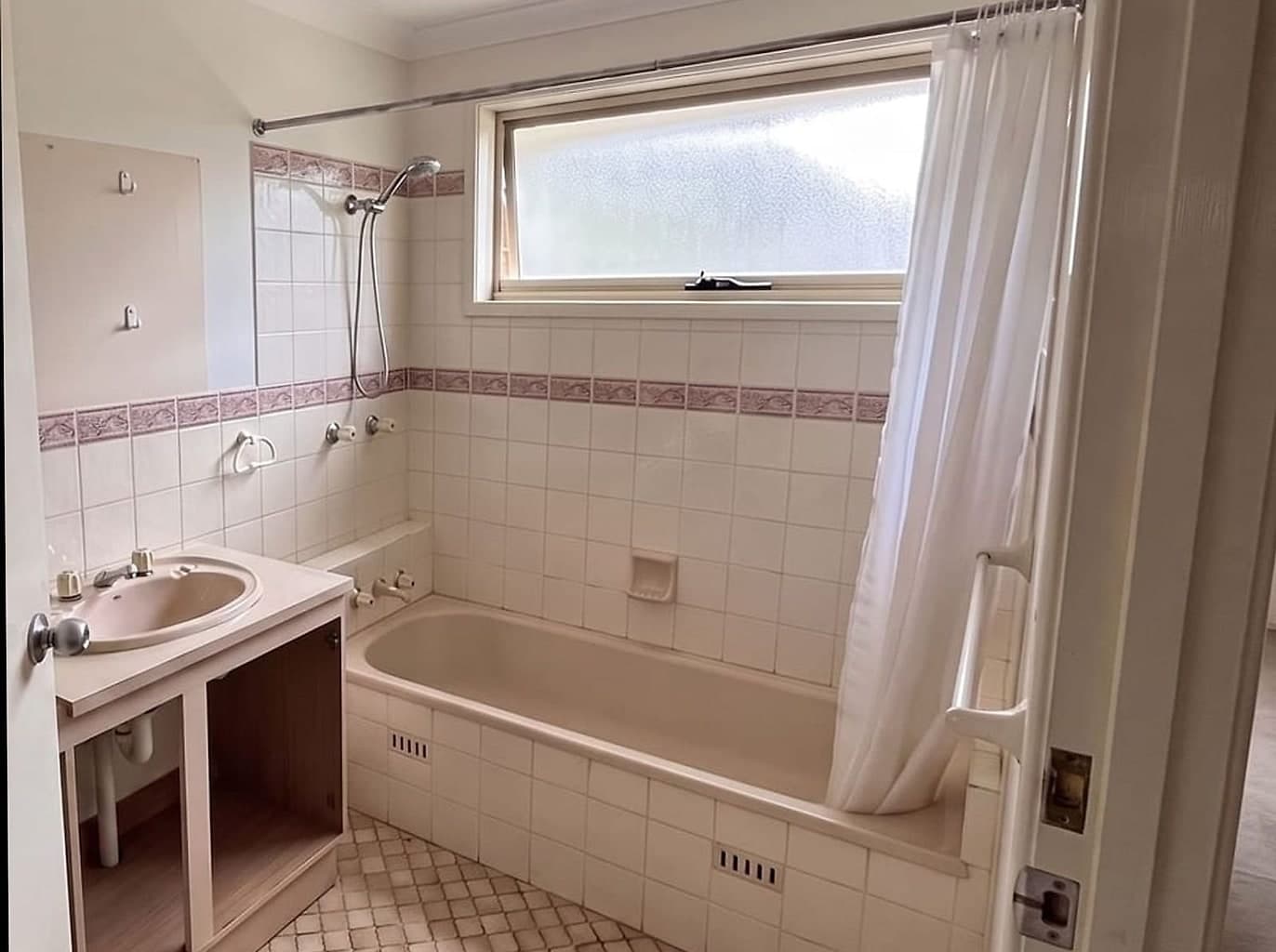 Dated family bathroom cleared for work, the door standing open, the vanity doors off and the mirror taken down