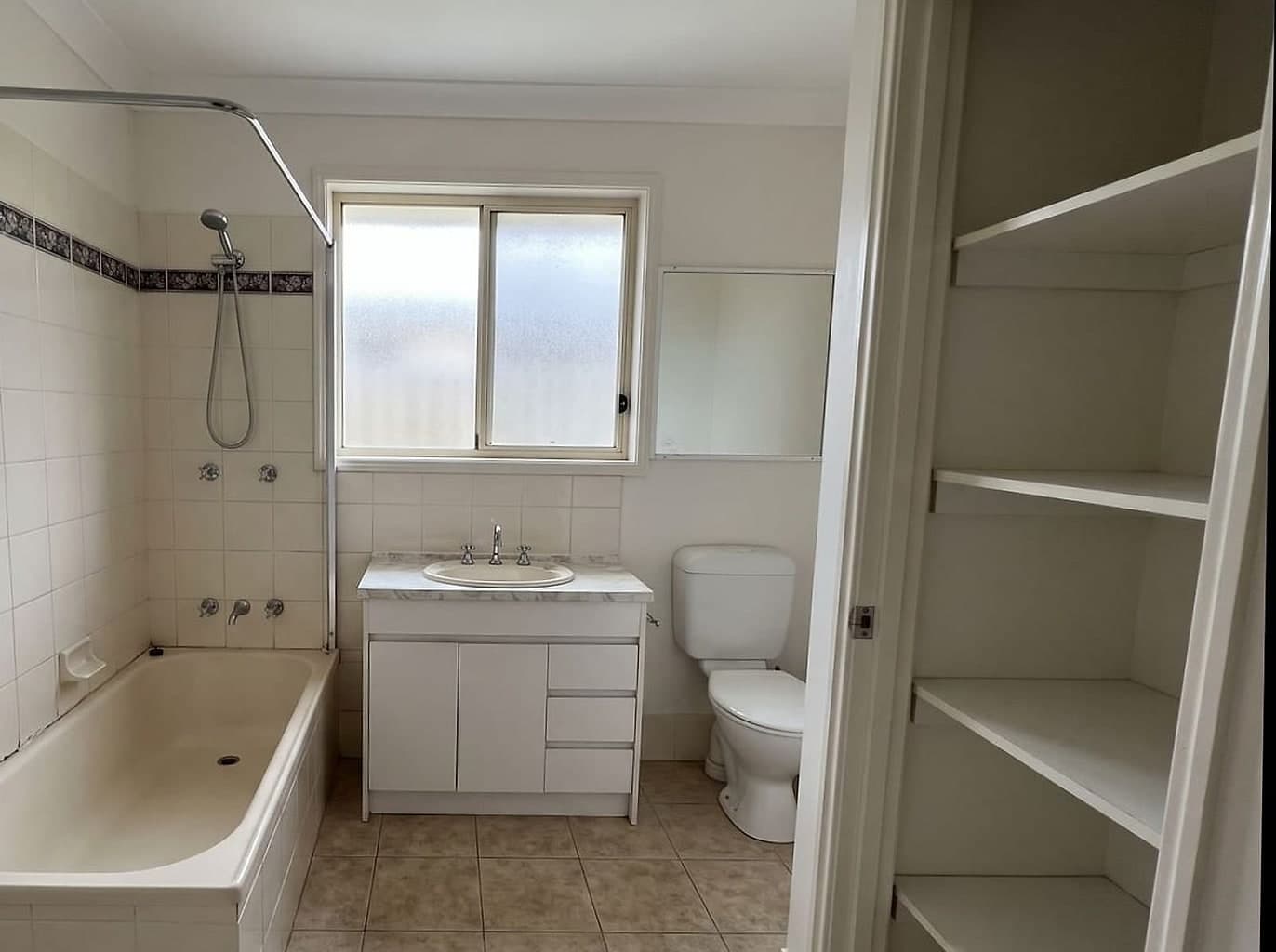 Cramped dated bathroom with the shower screen taken off the bath and the linen cupboard doors removed