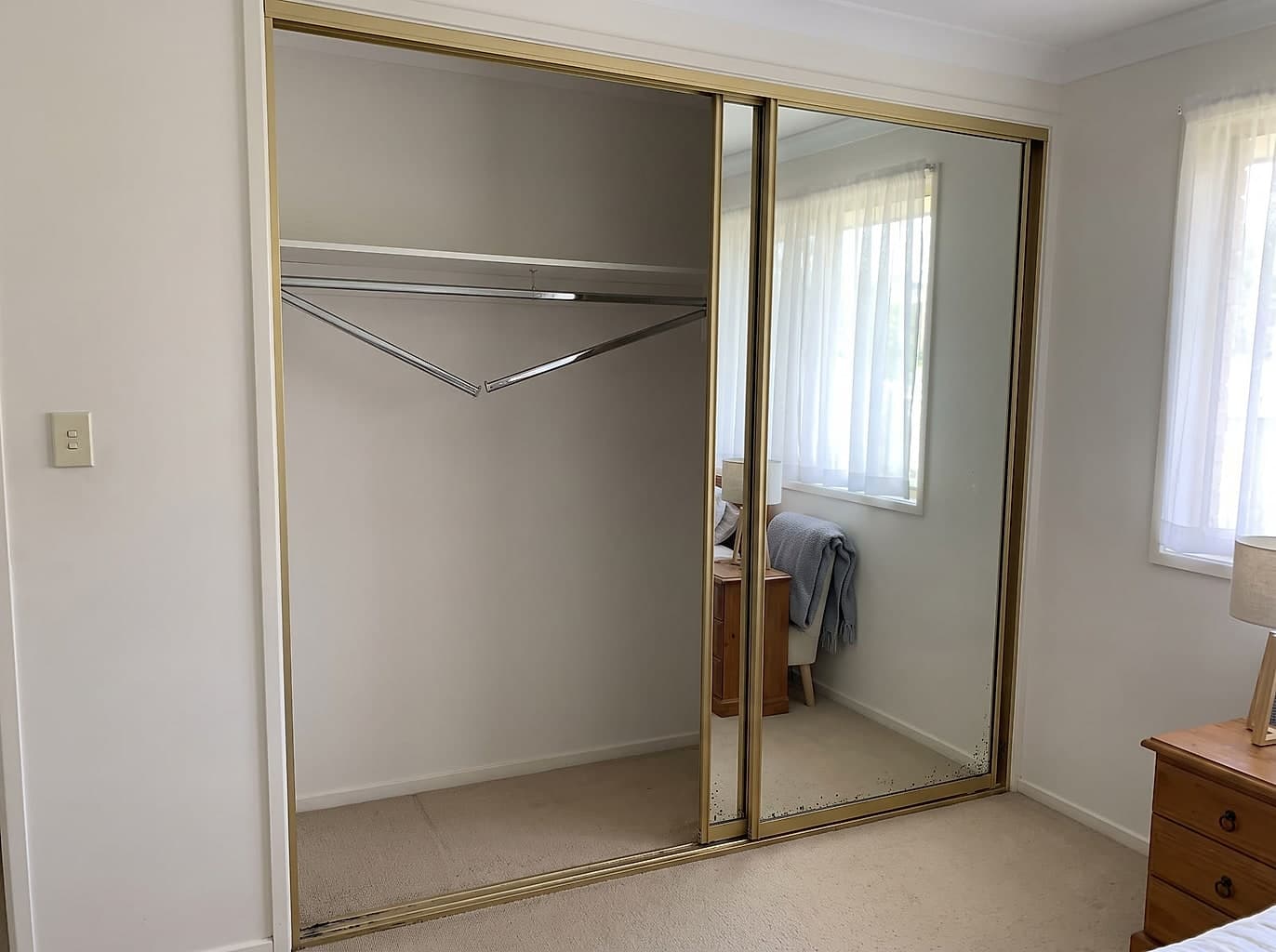 Dated wardrobe with gold-framed mirrored doors, one off its track and the mirror silvering spotted