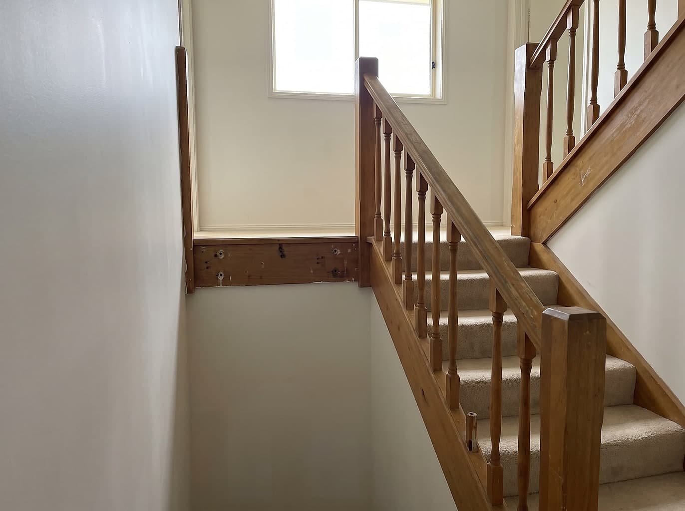 Dated timber staircase balustrade with turned spindles, a section unbolted and removed leaving bare fixing holes