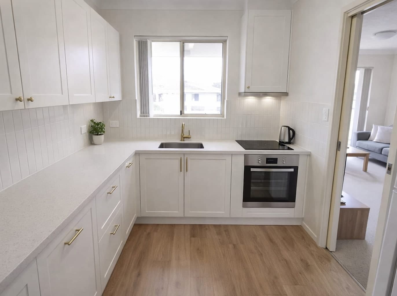 The same kitchen with white cupboards, a stone benchtop, new splashback and timber-look flooring