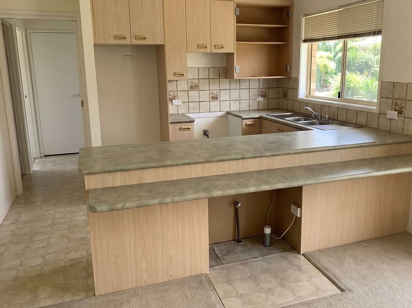 Dated peninsula kitchen with the dishwasher pulled out and a cupboard door taken off