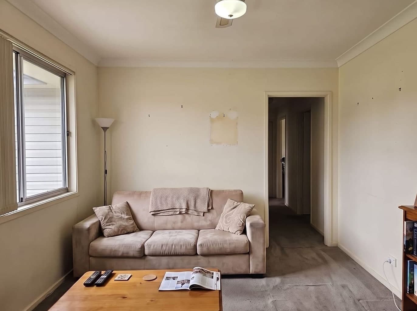 Living room with yellowed faded walls, filled patches and picture-hook holes, overdue for painting