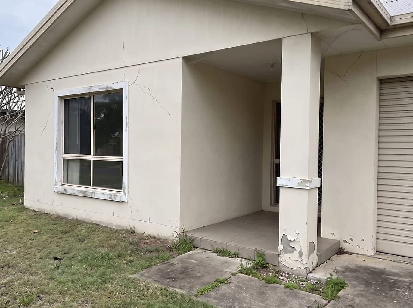 Faded rendered house front streaked with dirt and blooming with green-black mould