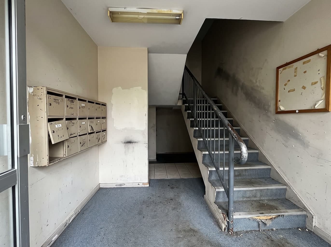 Tired unit block lobby with scuffed walls, worn carpet and a chipped handrail
